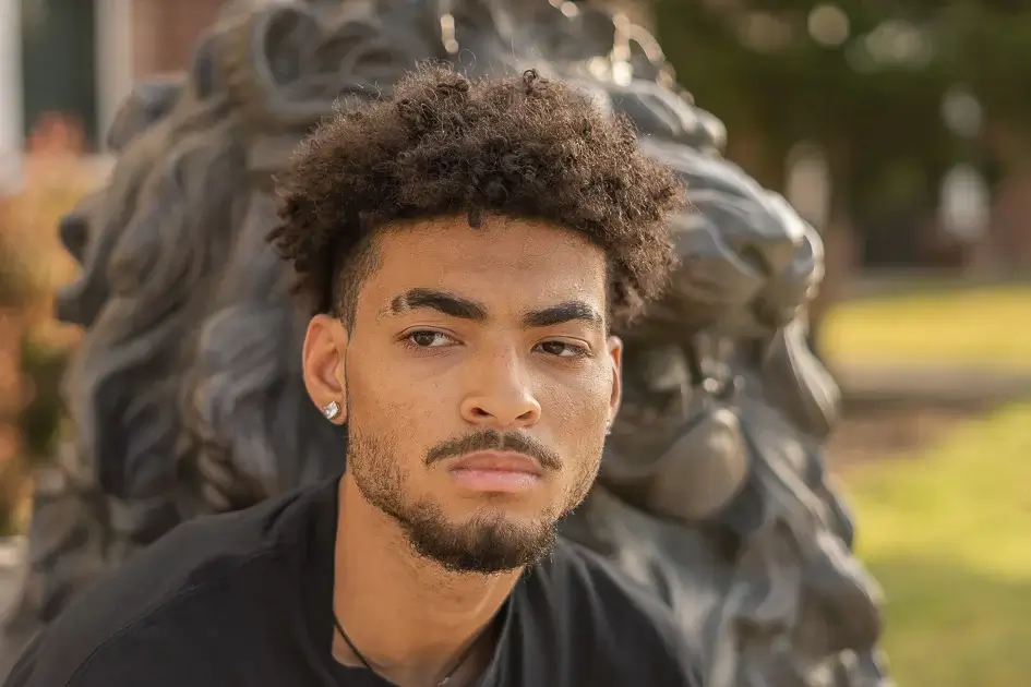 Senior mini sessions. Headshot photo of a high school senior with a calm serous expression, looking into the distance. He is sitting in front of a statue of a lion, his high school mascot.