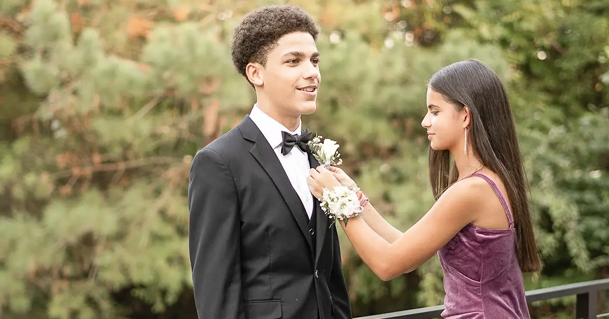 Homecoming dance photos. Image of a high school male and female. The female is pinning the boutonniere on the male's suit lapel.